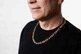 A person wearing a black shirt and a Two-Tone 10k Gold Plated Curb Chain necklace. The background is white. The person's head is turned to the left, and the face is partially visible.
