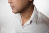 Close-up of a person wearing a white button-up shirt, shown from the side with the face partially visible and adorned with Solid 18k Yellow Saudi Gold Chains 2.5g. The background is plain and light in color.