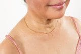 Close-up of a smiling person wearing a pink top, showing the neck and lower face adorned with a Yellowtone 14K GP Small Chain. The photograph highlights skin texture and natural complexion.