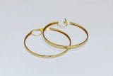 Two gold hoop earrings placed next to each other on a white surface.