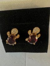 A pair of 18k Yellow-Gold Garnet & Diamond Earrings featuring a design that resembles a flower or a knot, with a central dark red gemstone, displayed on a black background.